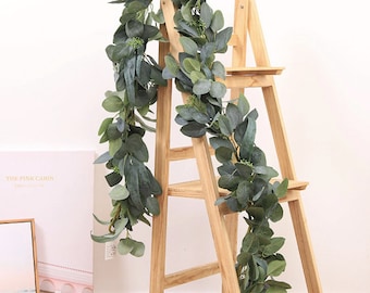 Op de afbeelding: Een lange, groene eucalyptus guirlande met kleine, ronde bladeren. De guirlande is over een houten ladder gehangen.