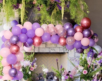 May include: A purple and pink balloon arch with rose gold balloons. The arch is decorated with confetti and is set up in front of a fireplace.