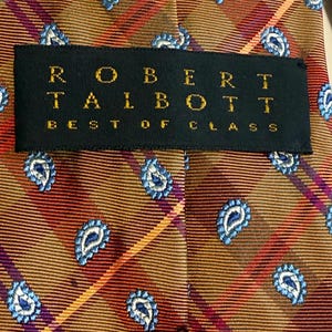 May include: Close-up of a Robert Talbott tie. The tie features a repeating paisley pattern in blue and white on a brown and orange plaid background. The label reads "ROBERT TALBOTT BEST OF CLASS."
