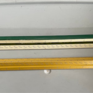 May include: Two rulers, one green and one yellow, with markings in inches. The green ruler has a metal edge and the yellow ruler has a wooden edge.
