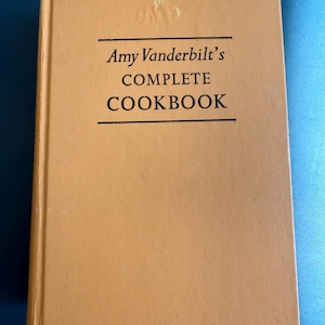 May include: A hardcover cookbook with a tan cover. The title "Amy Vanderbilt's COMPLETE COOKBOOK" is printed in black, centered on the cover. The book appears to be in good condition, with slight wear visible.