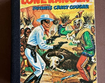 May include: A vintage comic book cover for "The Lone Ranger Outwits Crazy Cougar." The illustration shows the Lone Ranger in a white outfit and mask, holding guns, confronting a Native American figure. The background depicts a desert landscape with teepees.