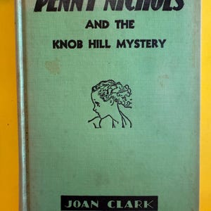 May include: A vintage book titled "Penny Nichols and the Knob Hill Mystery" by Joan Clark. The book has a light green cover with black text and a black illustration of a woman's profile. The book is slightly worn.