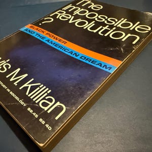 Op de afbeelding: Een hardcover boek met de titel "The Impossible Revolution?" van Lewis M. Killian. De omslag is donker met witte tekst en een blauwe, oranje en zwarte streep. De ondertitel is "Black Power and the American Dream."