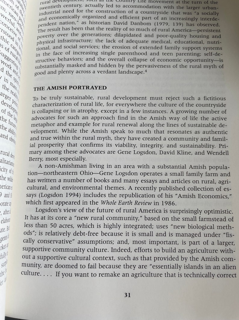 Puede incluir: Una imagen en blanco y negro de un libro con el t&iacute;tulo "Amish Economics" impreso en la portada. El libro est&aacute; abierto en una p&aacute;gina con texto sobre el estilo de vida Amish y c&oacute;mo se relaciona con el desarrollo rural.