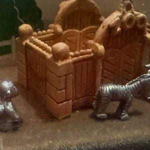 May include: A miniature scene featuring a small, detailed building with a gate and a zebra figurine. A small, seated figure is also present. The scene is set on a brown surface.