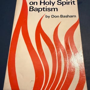 May include: A paperback book titled "A Handbook on Holy Spirit Baptism" by Don Basham. The cover features a white background with stylized red flame-like designs. The book is rectangular and appears to be in good condition.