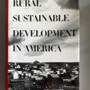 Puede incluir: Portada de libro con una foto en blanco y negro de un pueblo peque&ntilde;o. El t&iacute;tulo es "Rural Sustainable Development in America" y el autor es "Yvonne Audirac".