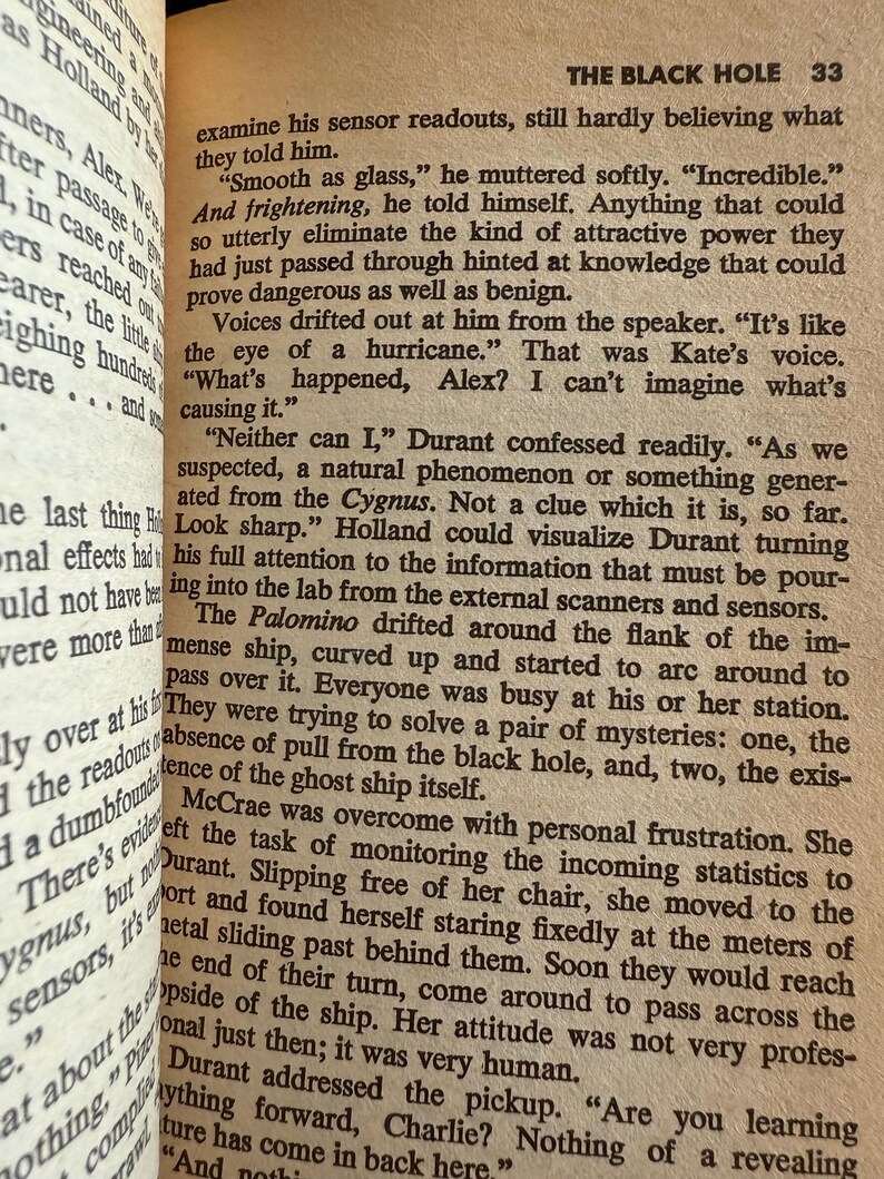 May include: Open book with text from a novel titled "The Black Hole." The text is in black font on aged, cream-colored paper. The page number "33" is visible. The text describes a science fiction scene with dialogue.