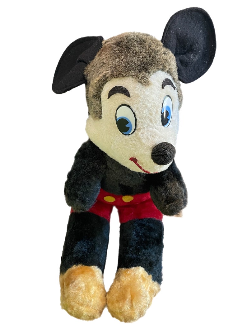 May include: A vintage plush Mickey Mouse toy with black ears, brown fur, white face, blue eyes, red shorts with yellow buttons, and tan feet.