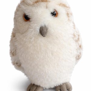 May include: A plush owl toy with soft, cream-colored feathers and brown accents. The owl has large, round orange eyes, a small gray beak, and gray feet. The toy is designed to resemble a snowy owl.
