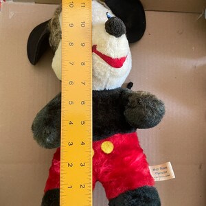 May include: A black and red plush Mickey Mouse toy with a yellow button on his shirt. The toy is 12 inches tall and has a black felt hat. The toy has a tag that reads "Walt Disney Character".