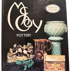 May include: A book titled "The Collectors Encyclopedia of McCoy Pottery" with a black cover. The cover features various McCoy pottery pieces, including a green frog, a cookie jar, and a pitcher. The book also has a sticker that says "UPDATED VALUES!"
