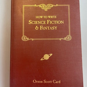 May include: A burgundy book with gold lettering on the cover. The title is "How to Write Science Fiction & Fantasy" by Orson Scott Card. A gold planet with rings is pictured below the title.