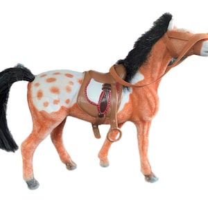 May include: A brown and white spotted toy horse with a black mane and tail. The horse is wearing a brown leather saddle with red stitching and a brown leather bridle.