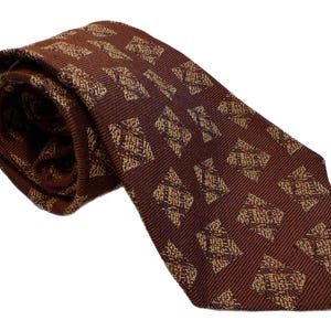 May include: A rolled-up brown tie with a repeating geometric pattern in a lighter shade of brown. The tie is made of a textured fabric and is displayed against a white background.