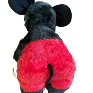 May include: Black and red plush Mickey Mouse toy. The toy is sitting on a white background. The toy has a black tail and large black ears.
