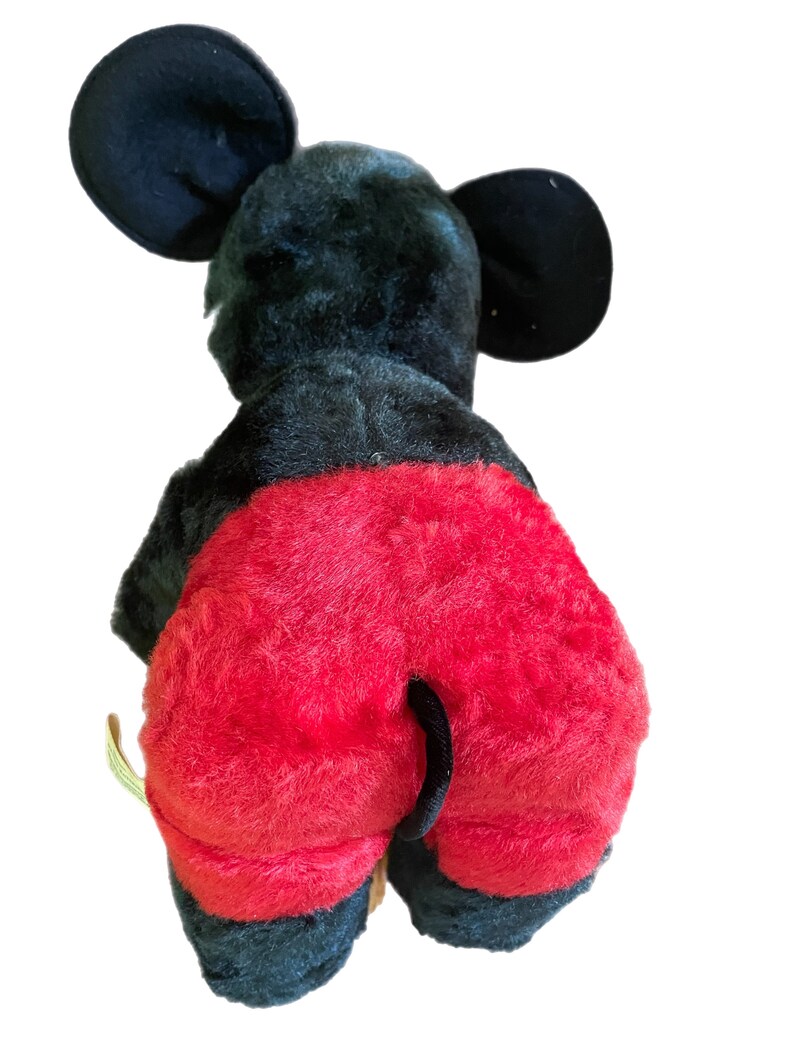 May include: Black and red plush Mickey Mouse toy. The toy is sitting on a white background. The toy has a black tail and large black ears.