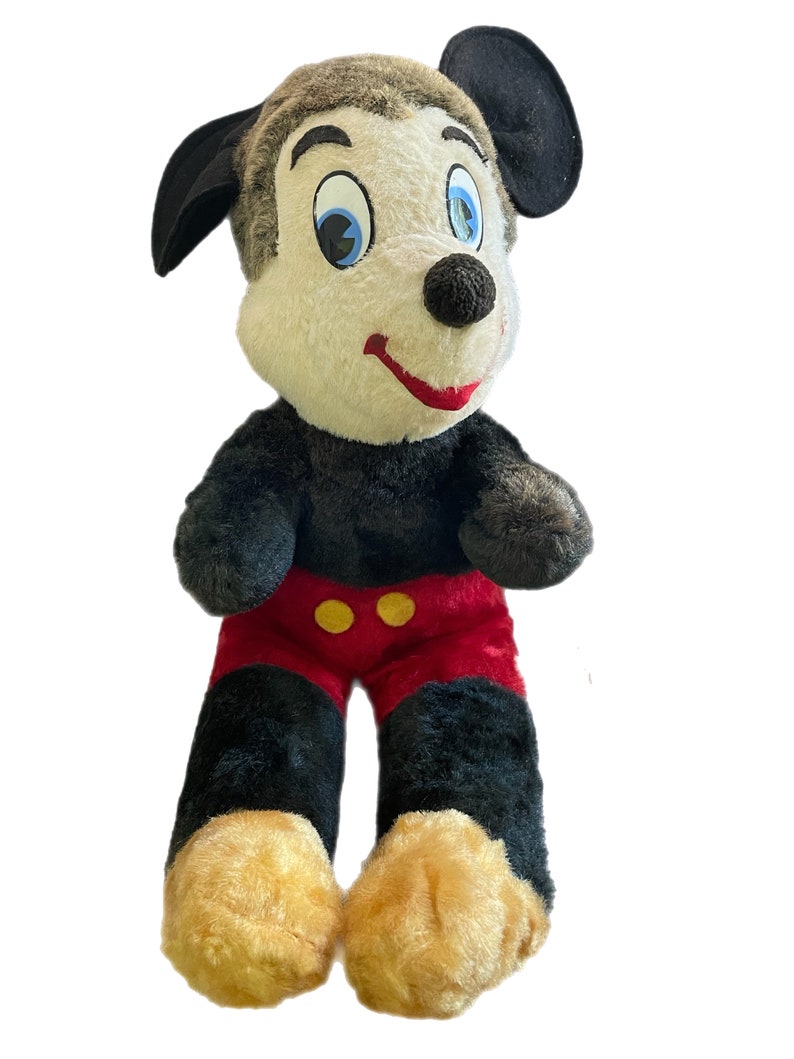May include: A vintage plush Mickey Mouse toy with black ears, black fur, red shorts with yellow buttons, and a white face with black eyes and a red mouth.