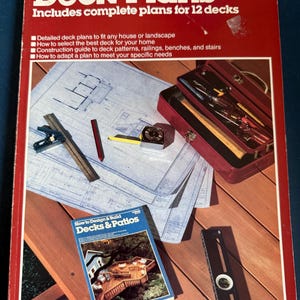 May include: A vintage book titled "Deck Plans" with the Ortho Books logo, featuring complete plans for 12 decks. The cover is red with white text and includes a list of features. A smaller book, blueprints, and tools are also visible.