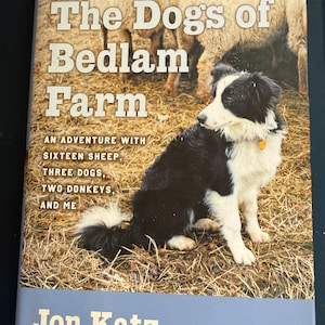 May include: Book cover for "The Dogs of Bedlam Farm" by Jon Katz. The cover features a black and white dog sitting in front of sheep. The title is in large white letters, with the author's name at the bottom.