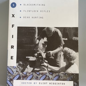 May include: A book cover with the title "FIRE" in large, bold letters. The cover features a black and white photograph of two people working on a metal object. The text "EDITED BY ELIOT WIGGINTON AND HIS STUDENTS" is printed below the photograph.