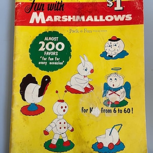 May include: A yellow book cover with the title "Fun with Marshmallows" and a price tag of £1. The book cover features illustrations of various marshmallow crafts, including a turkey, a robot, a bunny, a clock, an angel, and a baby carriage. The book advertises almost 200 favours for every occasion.