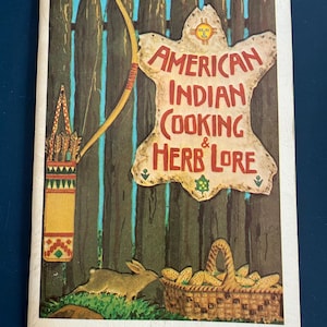 May include: Vintage book cover featuring the title "American Indian Cooking & Herb Lore" in red text on a tan background. The cover includes a bow and arrow, a quiver, a rabbit, and a basket of corn. A wooden fence and blue sky are in the background.