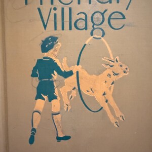 May include: A tan hardback book titled Friendly Village from The Alice and Jerry Books series. The cover features a teal illustration of a child in a beret holding a hoop for a tan goat to jump through, with teal text printed at the top and bottom.
