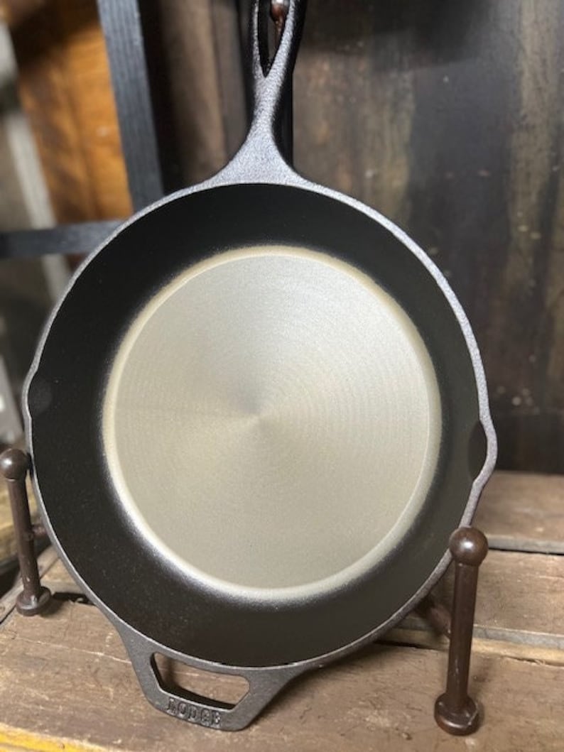 May include: A black cast iron skillet with a smooth, gray interior. The skillet has a long handle and is made by Lodge.