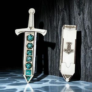 May include: A wooden sword-shaped dice holder with teal dice inside, next to a matching box. The sword has a detailed hilt and a compartment for the dice. The box features a decorative design and a symbol.