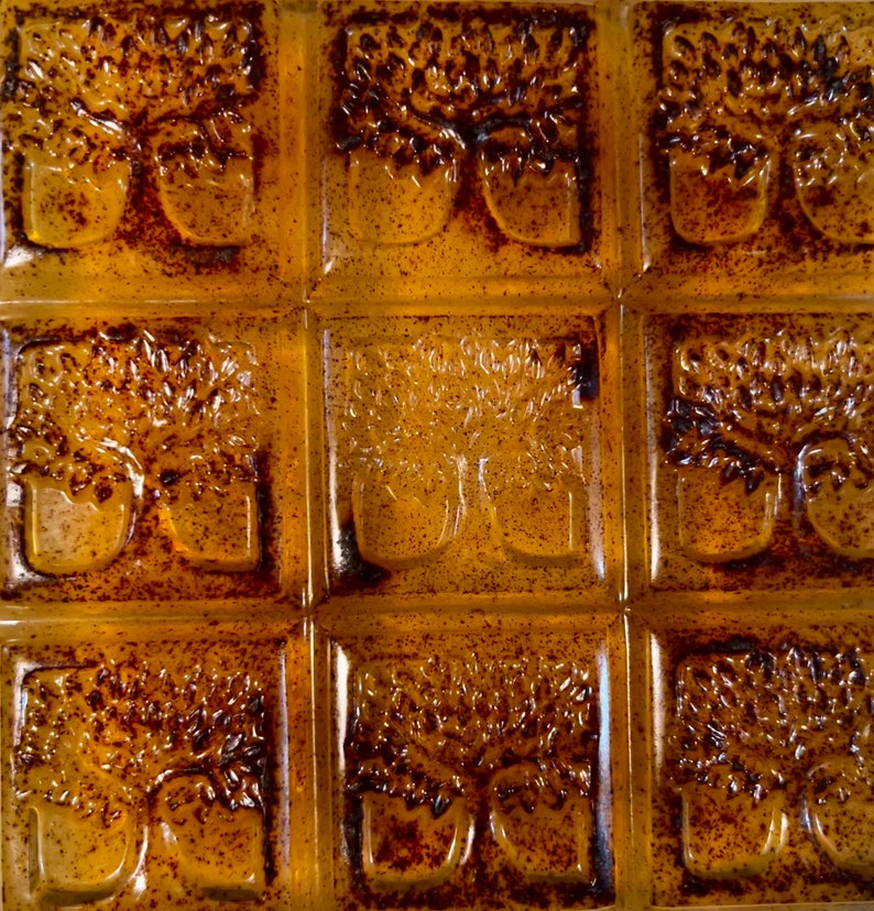 Pode incluir: Um conjunto de nove azulejos de vidro &acirc;mbar com um desenho em relevo de uma &aacute;rvore com dois troncos. Os azulejos est&atilde;o dispostos em uma grade de 3x3.