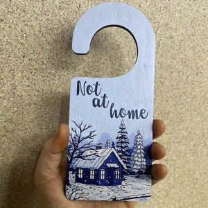 May include: A blue and white wooden door hanger with a snowy winter scene and the text "Not at home".