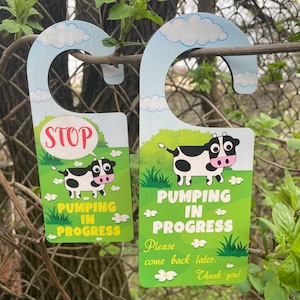 Puede incluir: Dos colgadores de puerta de madera con un diseño de vaca de dibujos animados. Los colgadores son verdes y presentan el texto "STOP" y "PUMPING IN PROGRESS". El texto del segundo colgador también dice "Por favor, vuelva más tarde. ¡Gracias!"