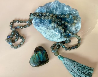 May include: A labradorite crystal heart and a labradorite beaded necklace with a teal tassel. The necklace is draped over a blue crystal cluster.
