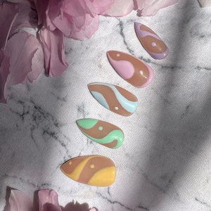 May include: Five fake nails with different abstract designs. The nails are painted in shades of brown, pink, blue, green, and yellow with white swirls and dots.