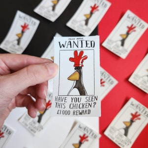 Puede incluir: Una mano sostiene un cartel de "Se busca" con un pollo de dibujos animados con un sombrero rojo. El cartel dice "Police Notice WANTED" y "Have you seen this chicken?" con un aviso de recompensa. Otros carteles similares están dispersos.