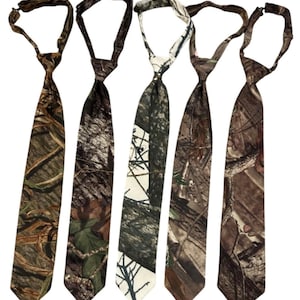 May include: Five camouflage neckties in shades of brown, green, and white. Each tie features a different woodland design, with varying patterns of leaves, branches, and bark. The ties are arranged vertically against a white background.