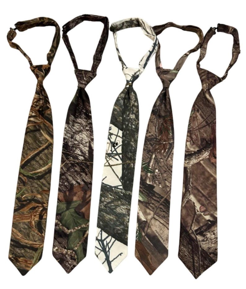 May include: Five camouflage neckties in shades of brown, green, and white. Each tie features a different woodland design, with varying patterns of leaves, branches, and bark. The ties are arranged vertically against a white background.