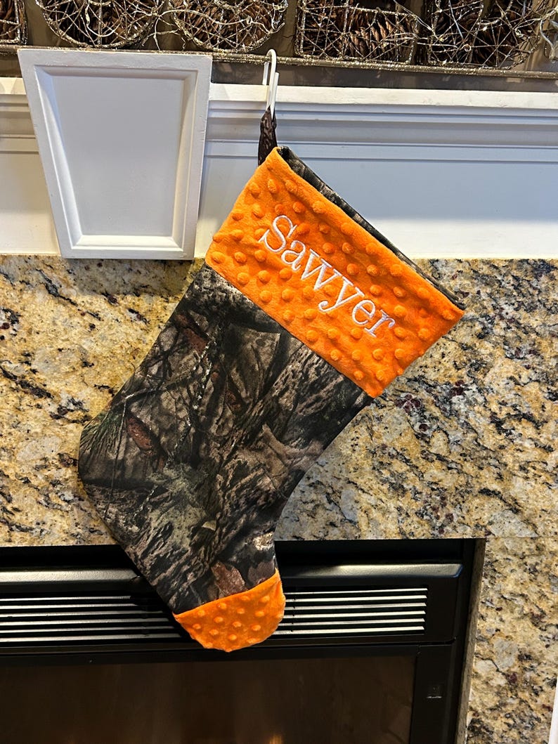 May include: A camouflage and orange Christmas stocking with the name "Sawyer" embroidered on the orange fabric.