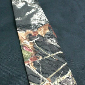May include: A camouflage patterned tie with brown, green, and white colours. The tie has a leaf and branch design.
