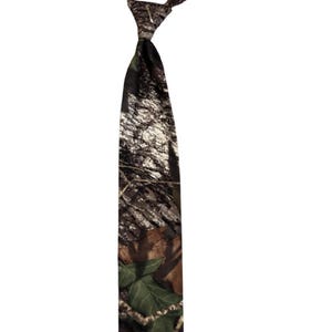 May include: A camouflage-patterned tie, displaying a mix of brown, green, and beige colours. The tie is knotted at the top, with the wider end hanging down. The fabric has a forest-like design, suitable for outdoor or hunting-themed clothing.