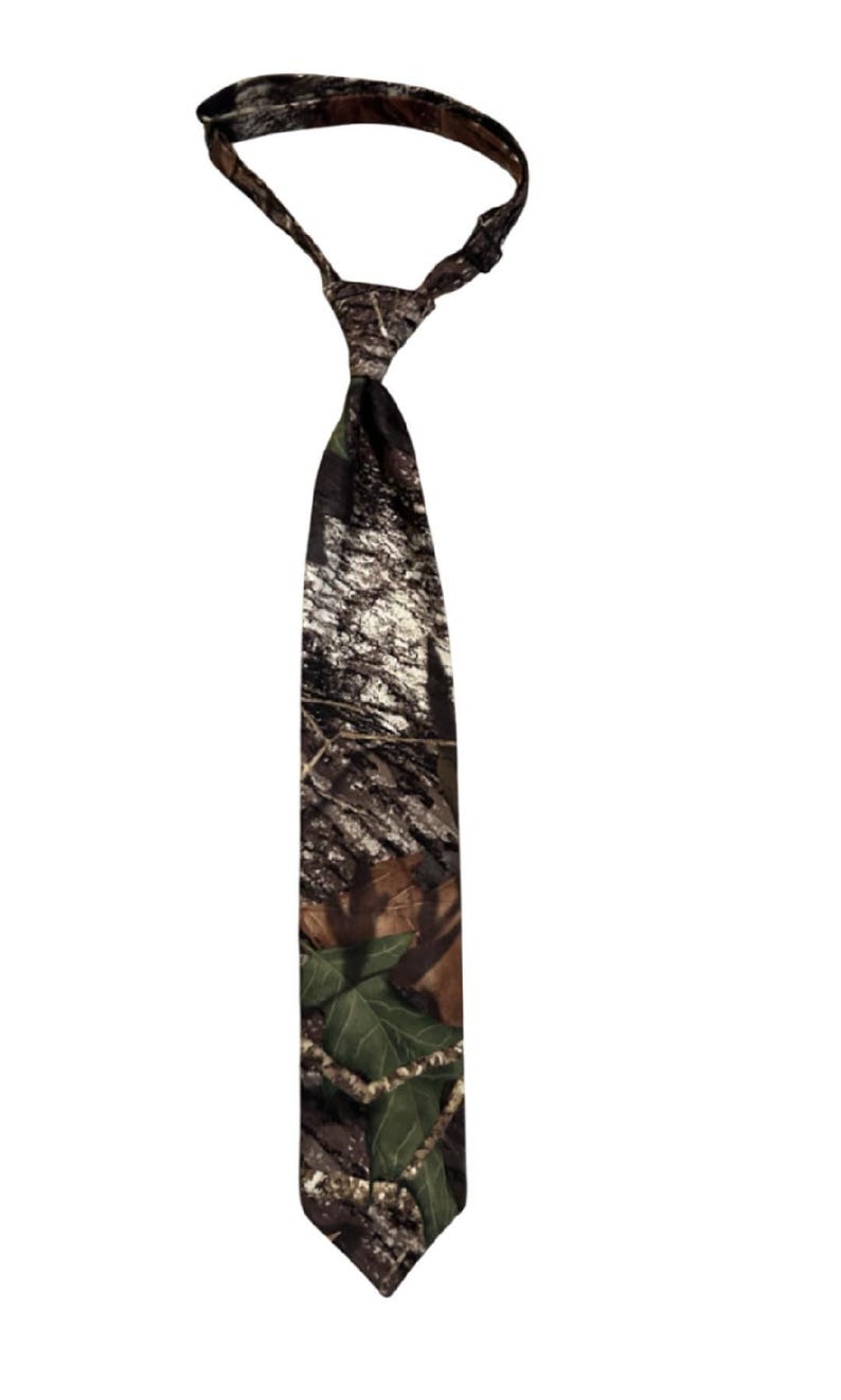 May include: A camouflage-patterned tie, displaying a mix of brown, green, and beige colours. The tie is knotted at the top, with the wider end hanging down. The fabric has a forest-like design, suitable for outdoor or hunting-themed clothing.