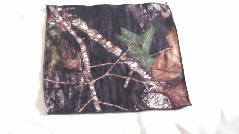 Puede incluir: Una tela de camuflaje con fondo negro y hojas y ramas marrones, verdes y blancas.