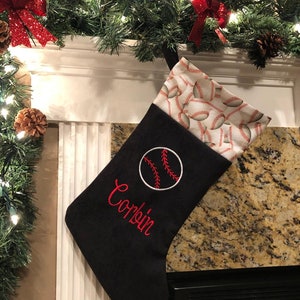 May include: Black Christmas stocking with a baseball design. The stocking has a baseball embroidered on the front with the name "Corbin" in red. The top of the stocking is patterned with baseballs.