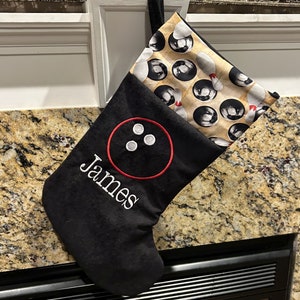 May include: Black Christmas stocking with a bowling theme. The stocking features a red embroidered bowling pin design with the name "James" in white. The top portion has a pattern of bowling pins and balls.