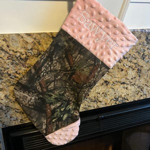 May include: A pink and brown camouflage Christmas stocking with the name "Sawyer" embroidered on the pink cuff.