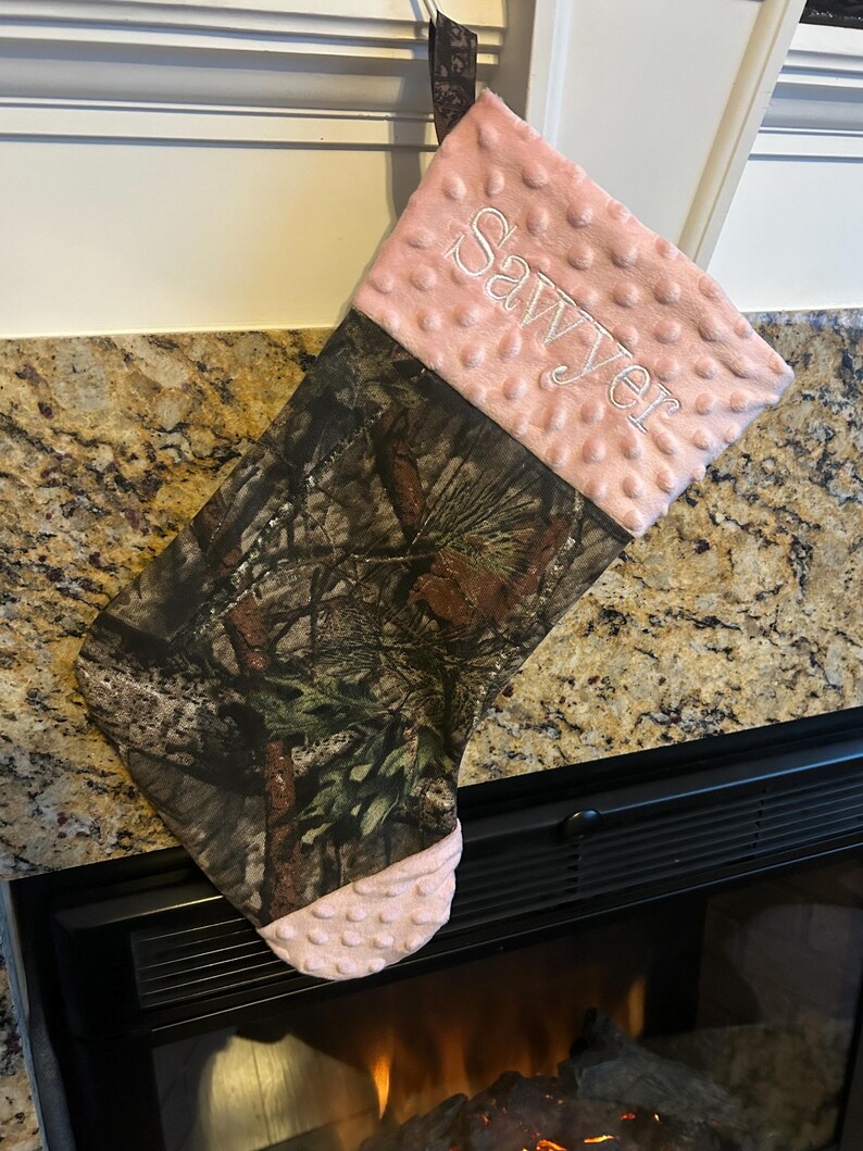 May include: A pink and brown camouflage Christmas stocking with the name "Sawyer" embroidered on the pink cuff.