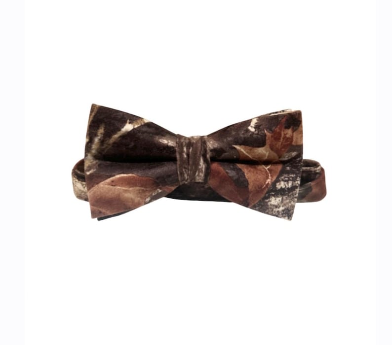 Puede incluir: Una pajarita marr&oacute;n con un estampado de camuflaje con hojas marrones, beige y blancas.