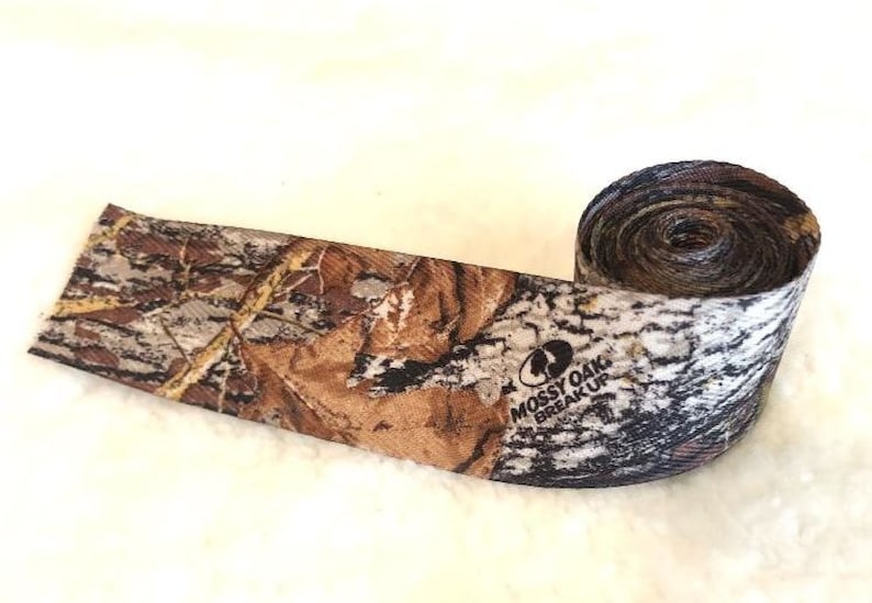 May include: A roll of camouflage fabric with a brown, tan, and black pattern. The fabric has the words "Mossy Oak Break-Up" printed on it.